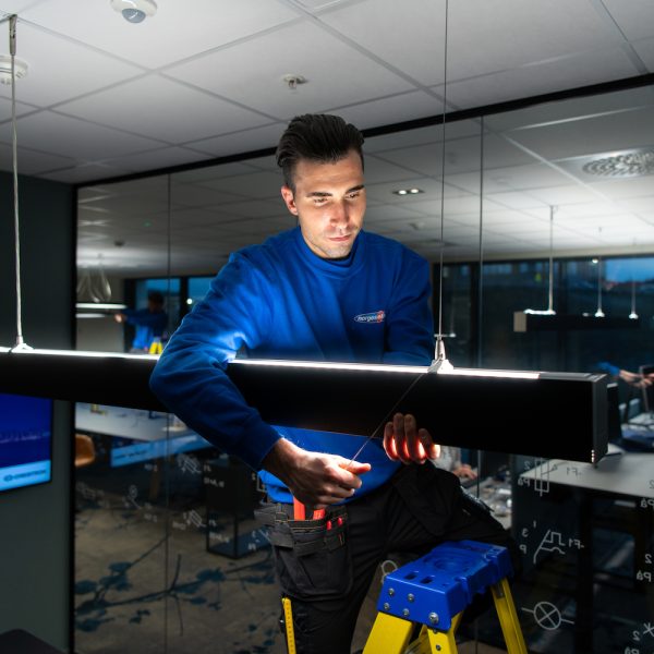 Elektriker monterer designlampe på møterom i moderne kontorbygg.